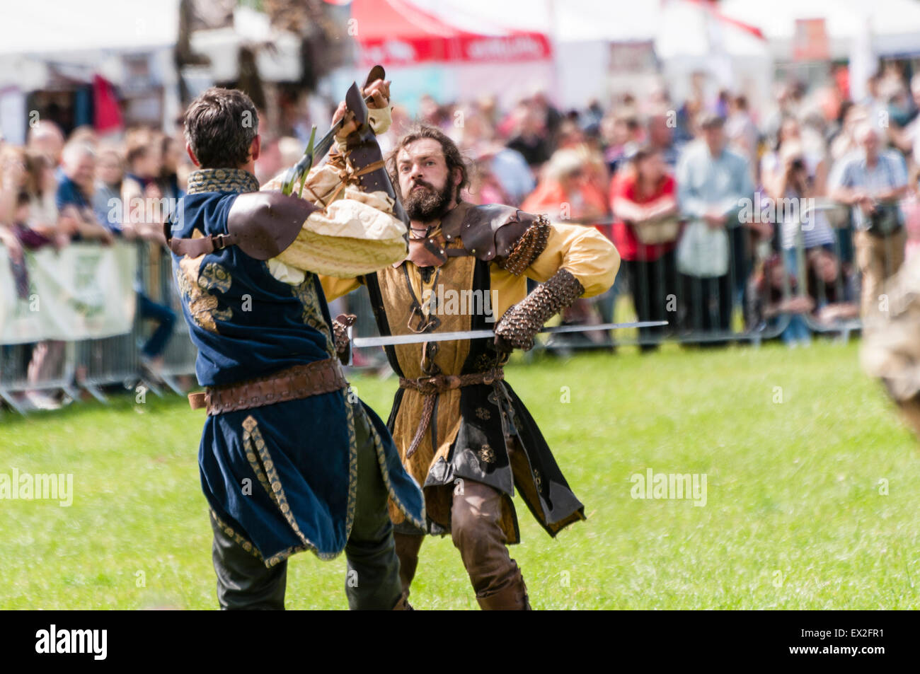 Men dressed as knights stage a battle for a crowd at an outdoor fair. Stock Photo