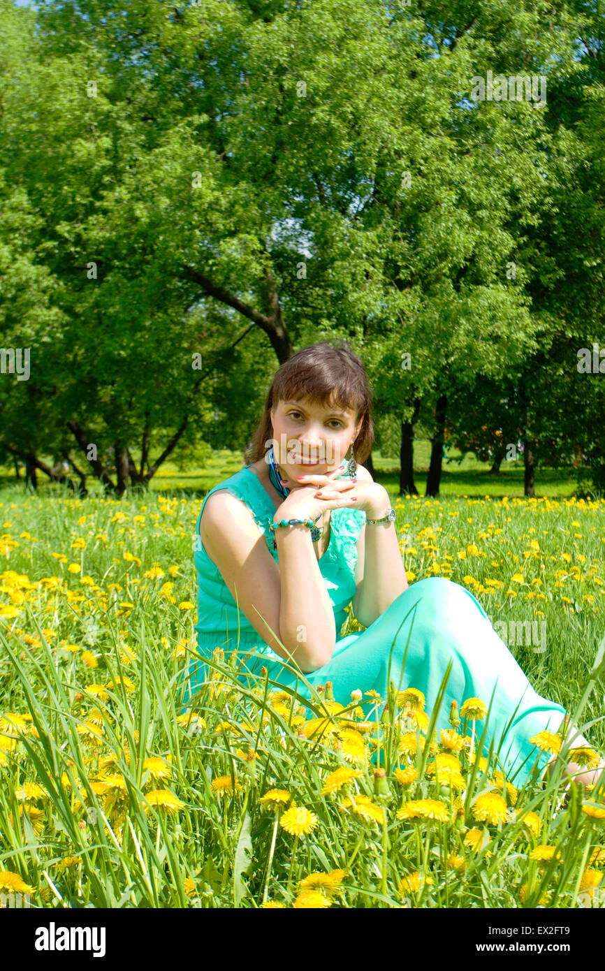 Pretty lady brunetter European sitting on meadow with yellow dandelions. Stock Photo