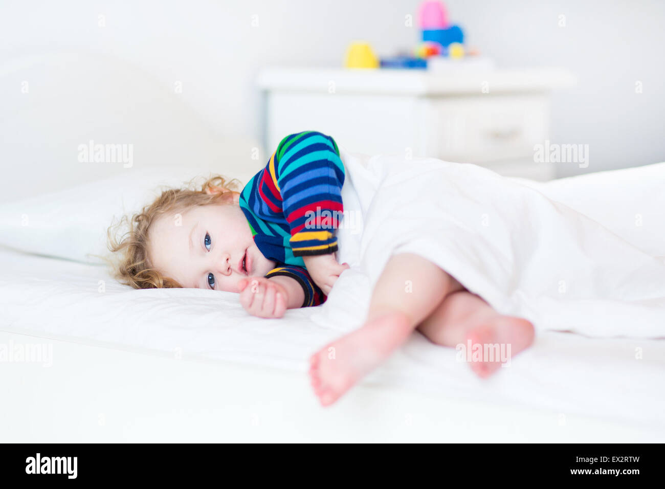 Adorable toddler girl waking up in the morning in a sunny white bedroom