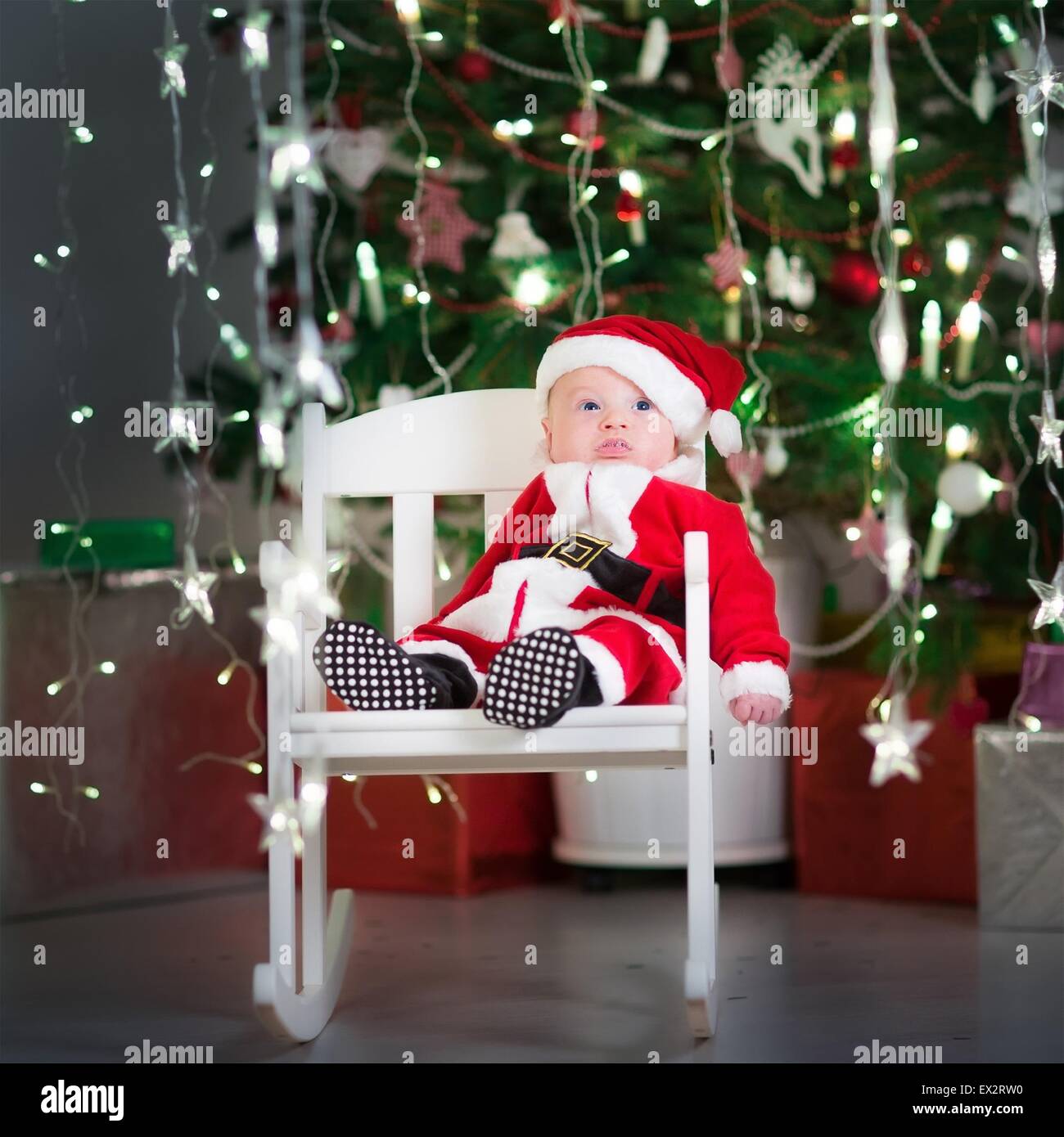 Cute newborn baby in a santa costume and hat sitting in a white rocking ...