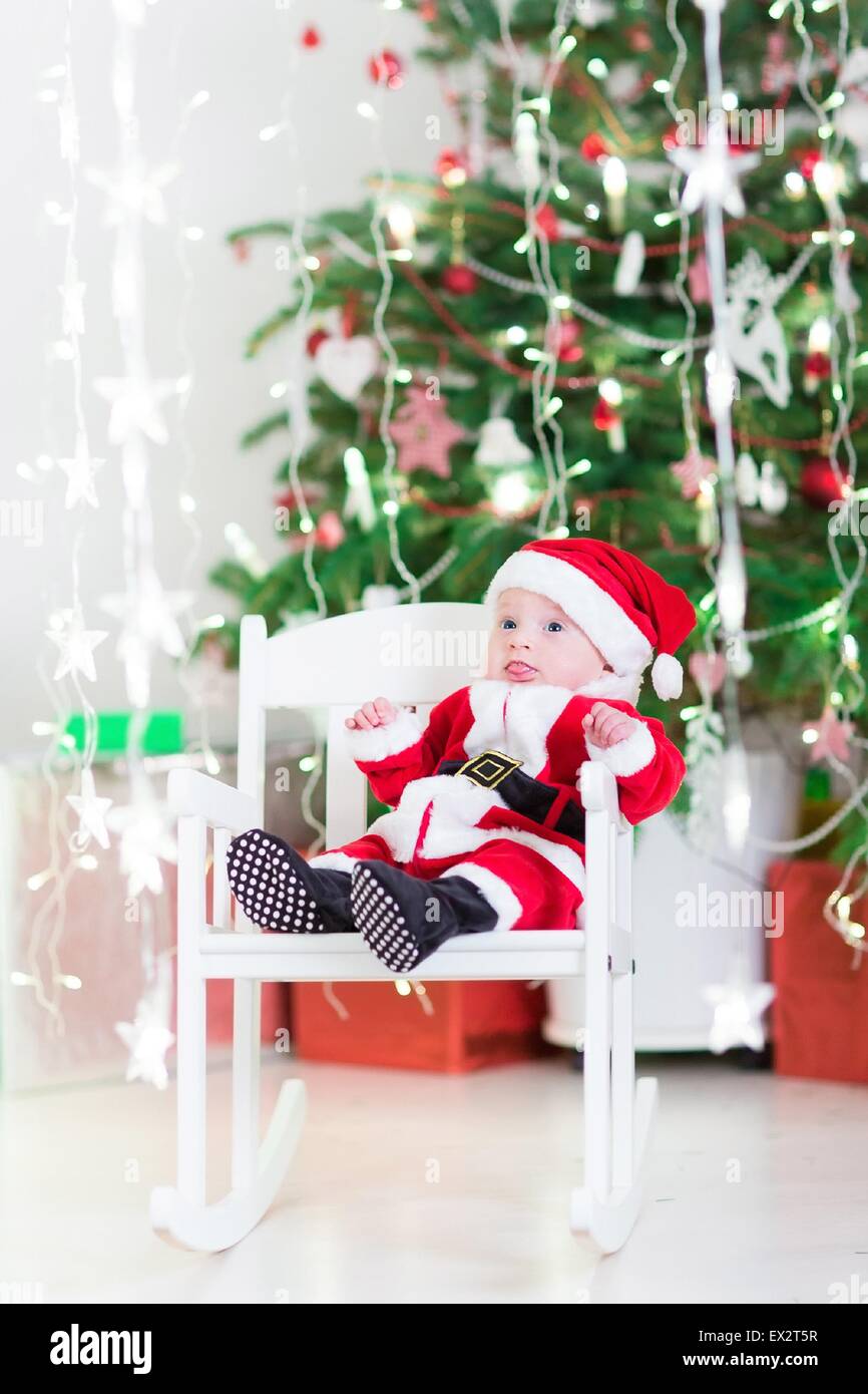 Smiling newborn baby boy in Santa costume sitting in a white rocking ...