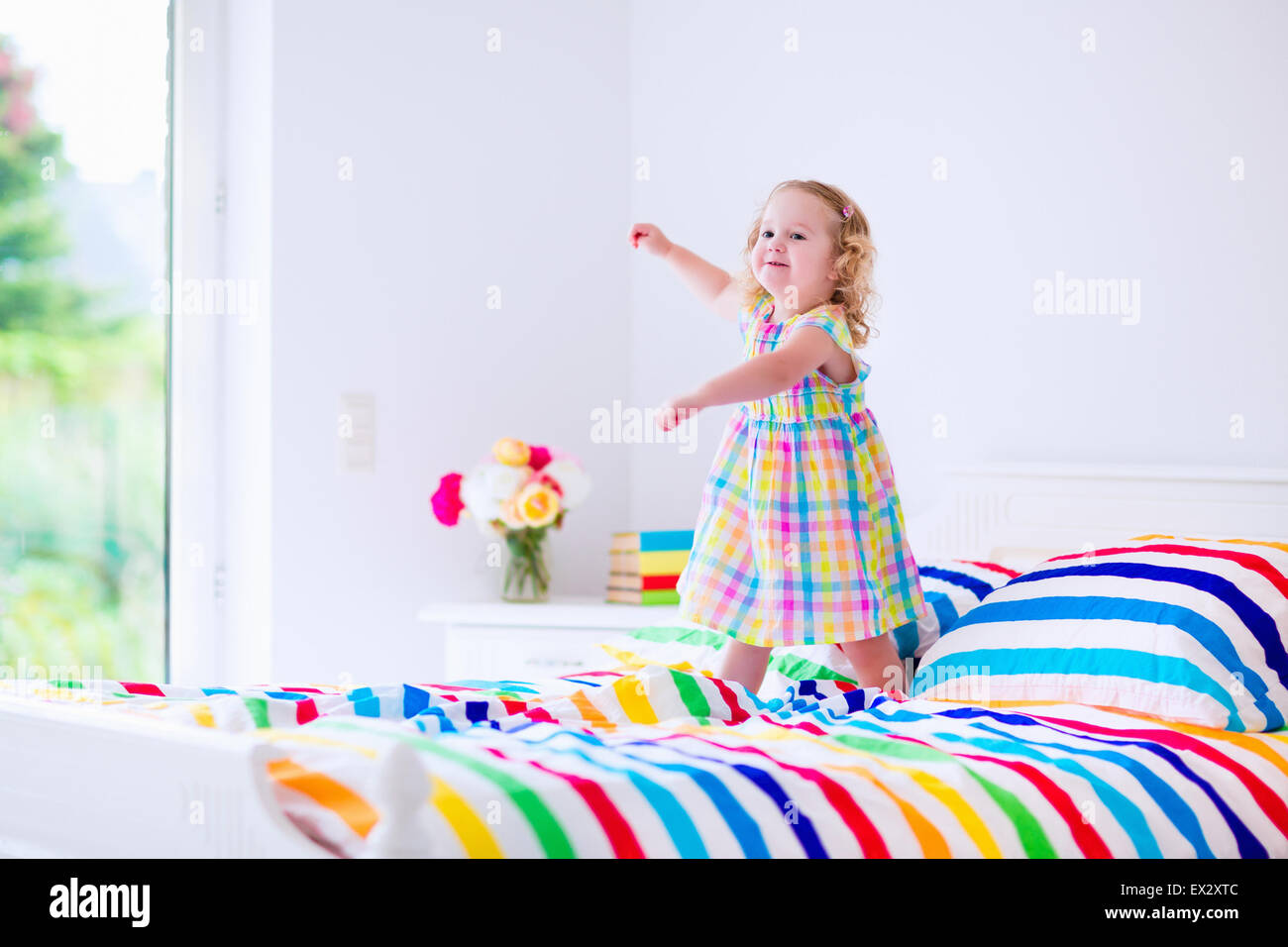 Children jump on a bed. Cute little girl jumping and dancing in a sunny white bedroom. Kids room