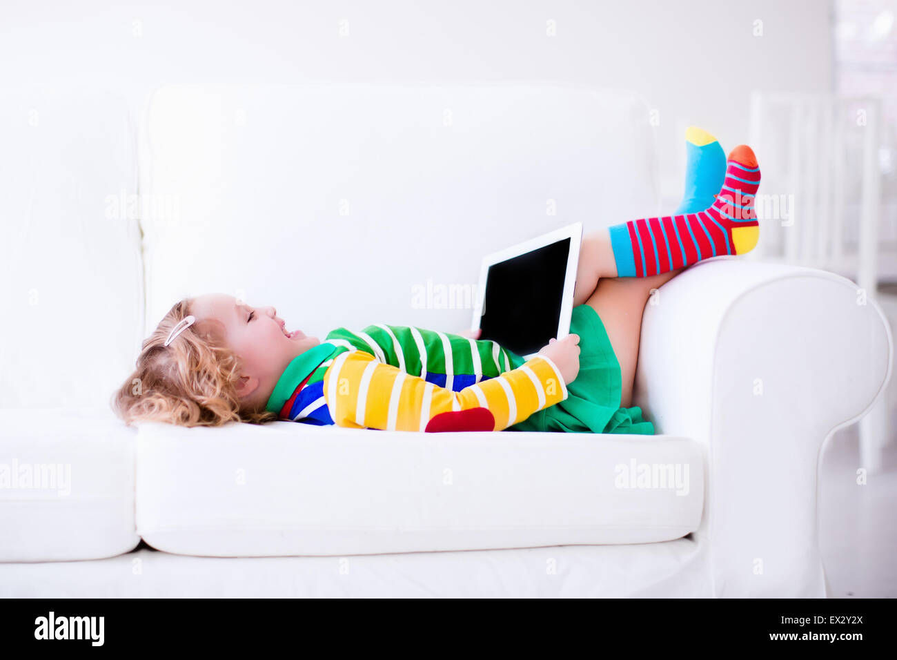 Little Girl Holding Tablet Pc Relaxing On A White Couch Kids