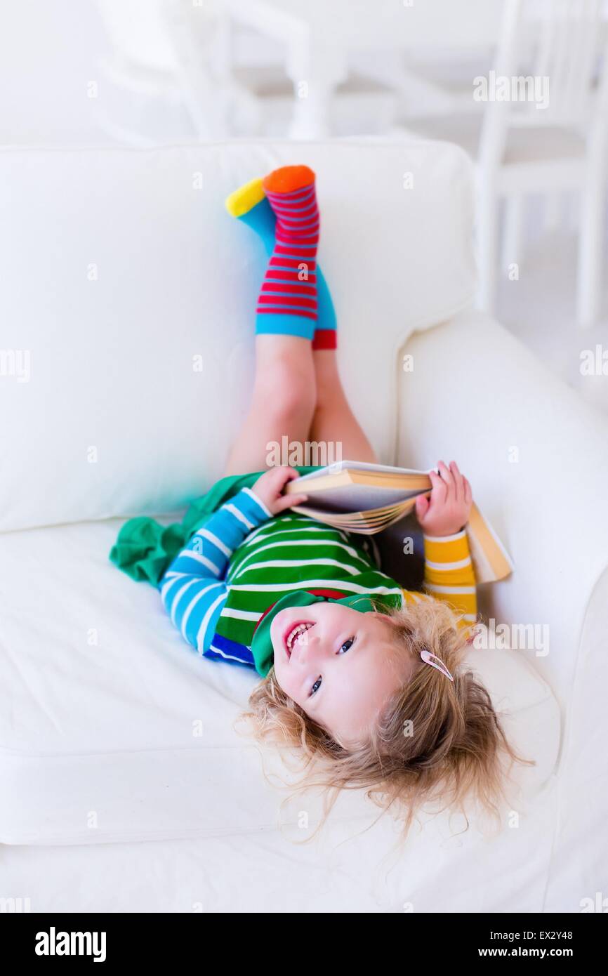 Little Girl Reading A Book Relaxing On A White Couch Kids Read