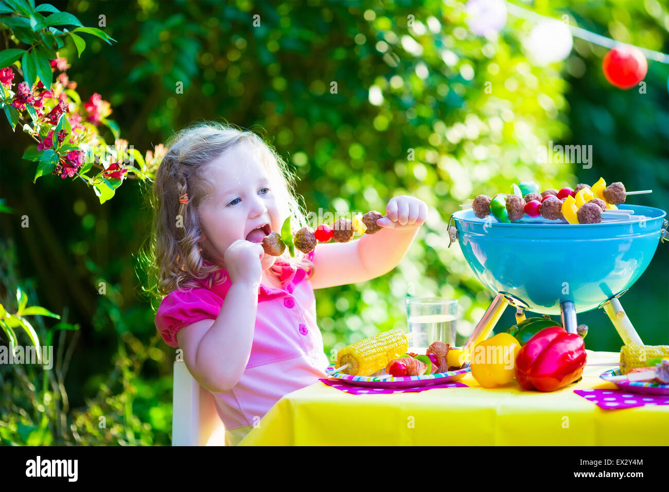 Children grilling meat. Family camping and enjoying BBQ. Little girl at barbecue preparing steaks, kebab and corn. Stock Photo