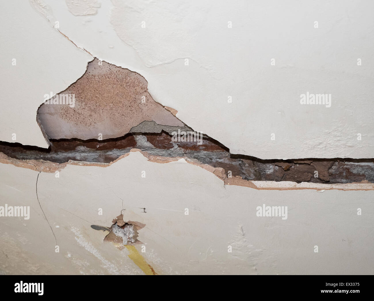 badly cracked plasterboard on interior wall showing bricks behind Stock Photo