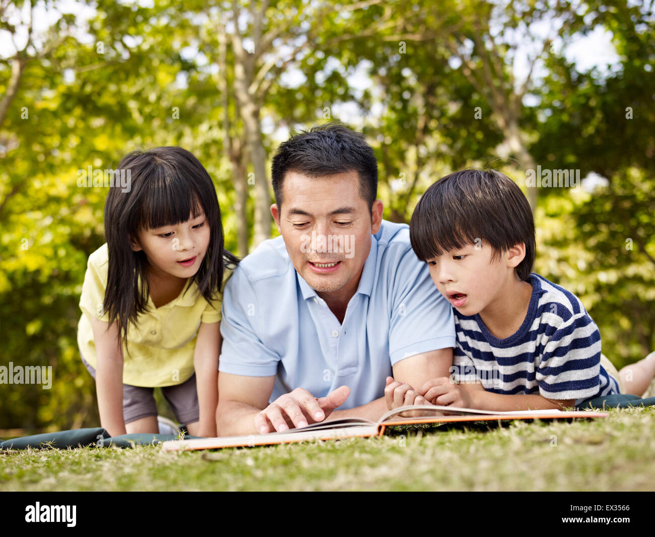 father and children reading a book outdoors. Stock Photo