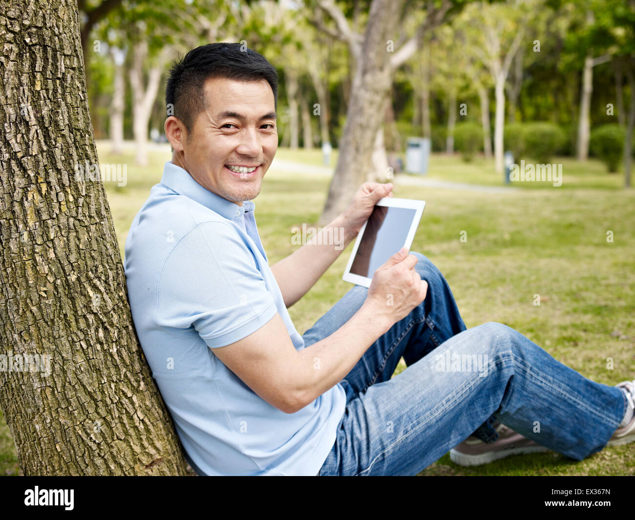 asian man in casual wear using tablet computer outdoors in park. Stock Photo