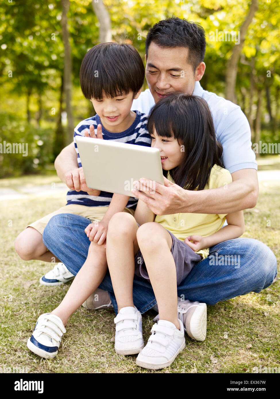 father and children using ipad in park Stock Photo