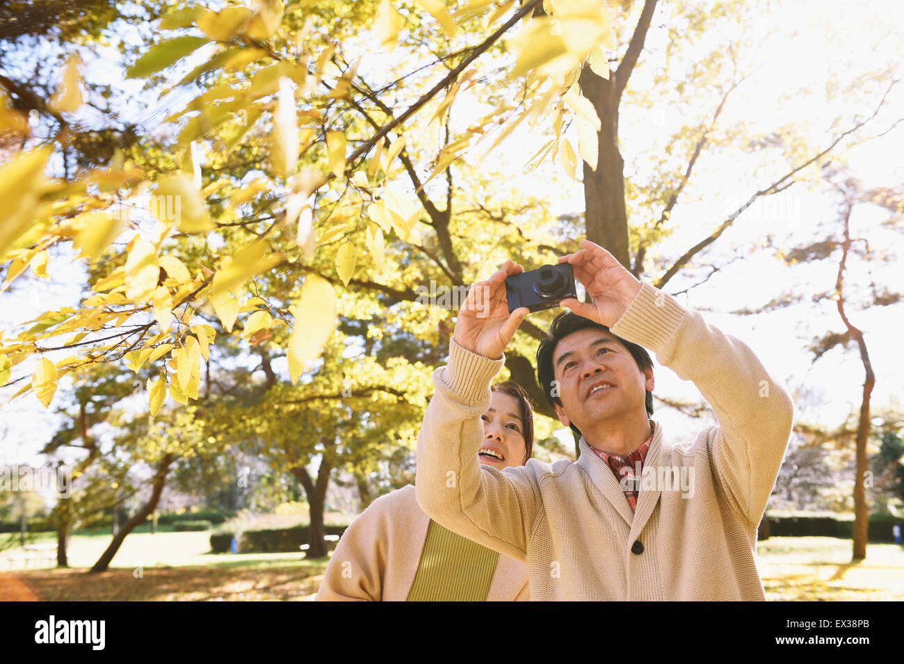 Senior Japanese couple taking pictures in a city park in Autumn Stock Photo