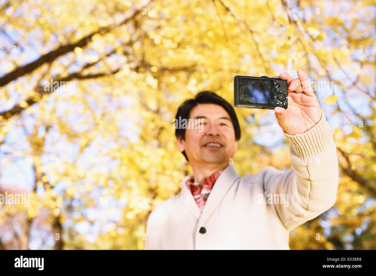 Senior Japanese man taking a selfie in a city park in Autumn Stock Photo