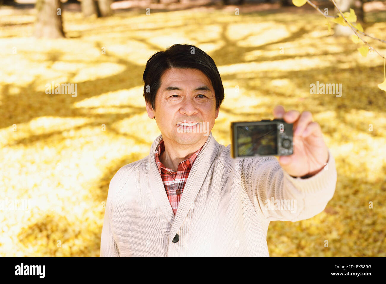 Senior Japanese man taking a selfie in a city park in Autumn Stock Photo