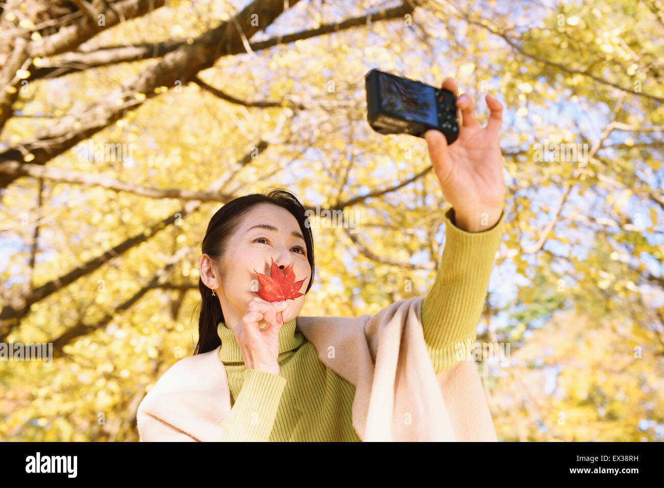 Senior Japanese woman taking a selfie in a city park in Autumn Stock Photo