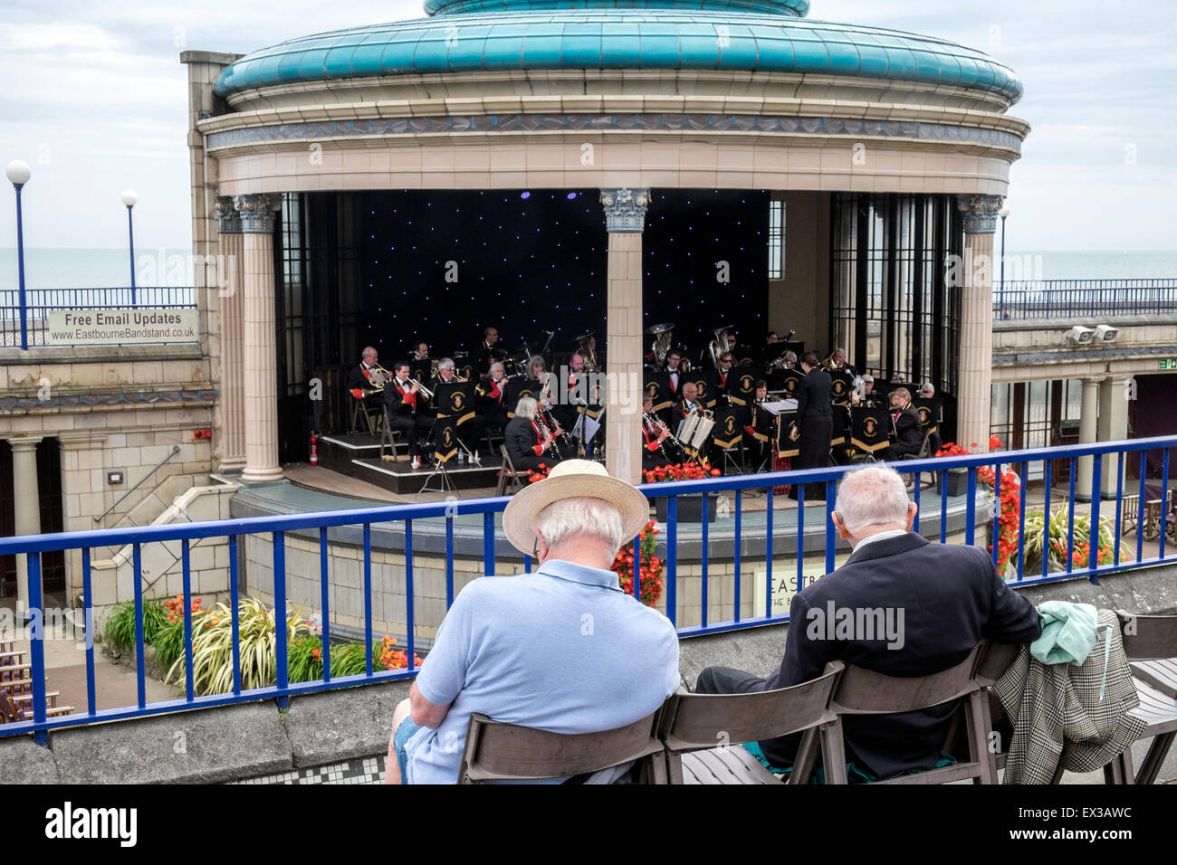 two seated elderly men watching a band playing music at Eastbourne Bandstand Stock Photo