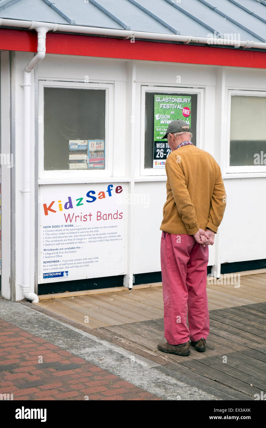 Old man looking at a notice advertising wrist bands for children inscribed with parents' details in case children get lost. Stock Photo