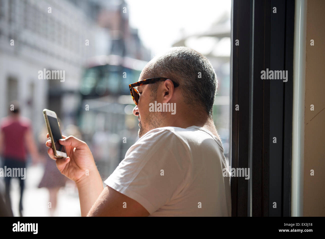 Man in pub drinking a pint of lager and checking his mobile phone Stock Photo