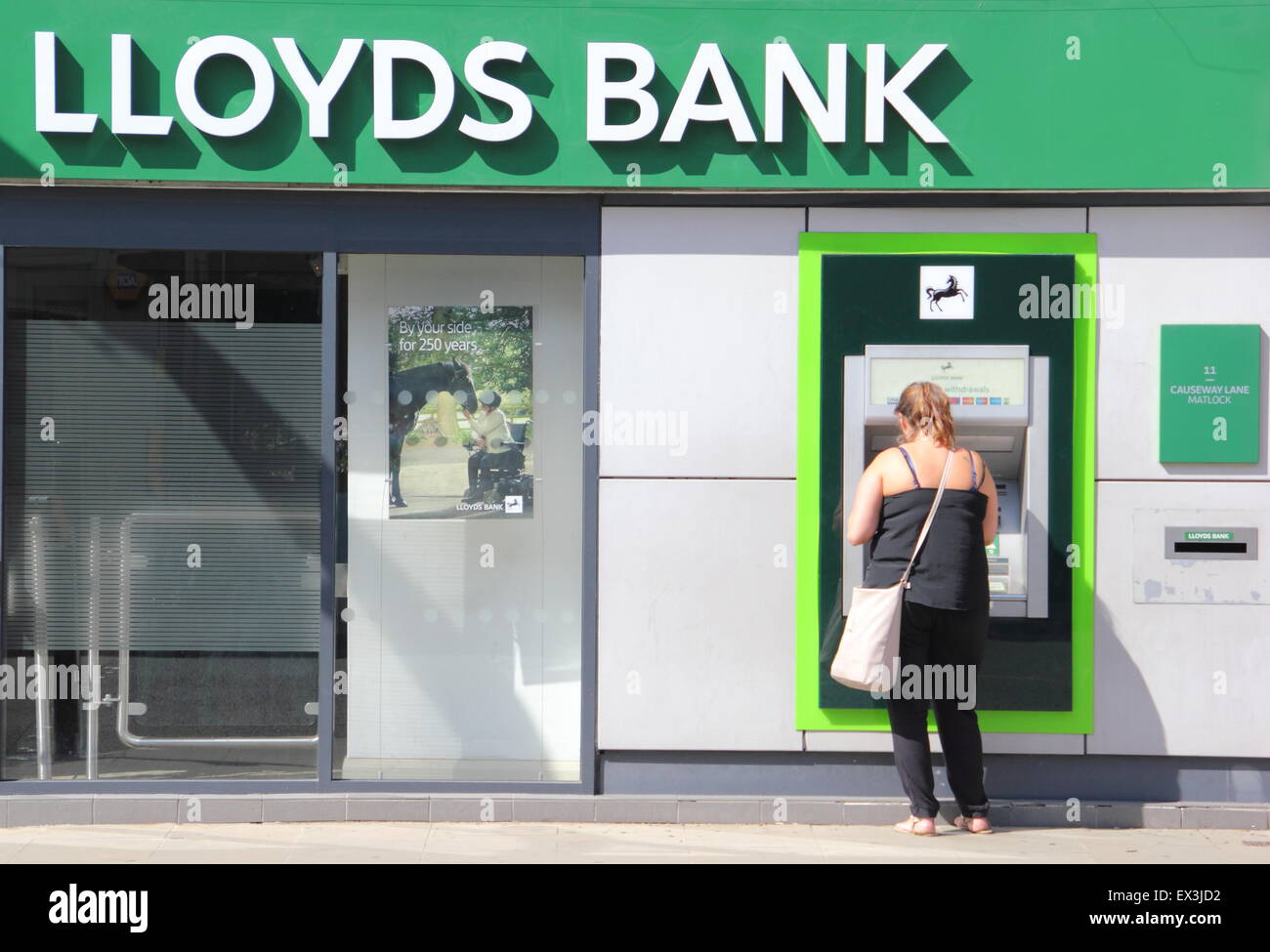 A woman uses an ATM cashpoint machine at a Lloyds Bank branch in Derbyshire England UK Stock Photo