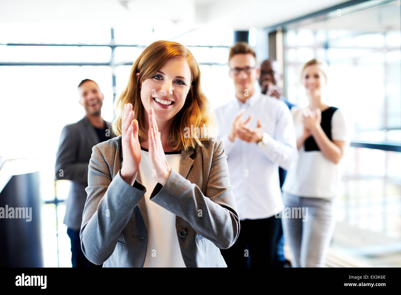 Young white female executive standing in front of colleagues clapping and smiling Stock Photo