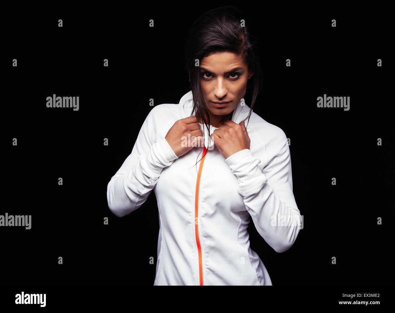 Portrait of confident young woman wearing sports jacket looking at camera against black background. Fitness female model. Stock Photo
