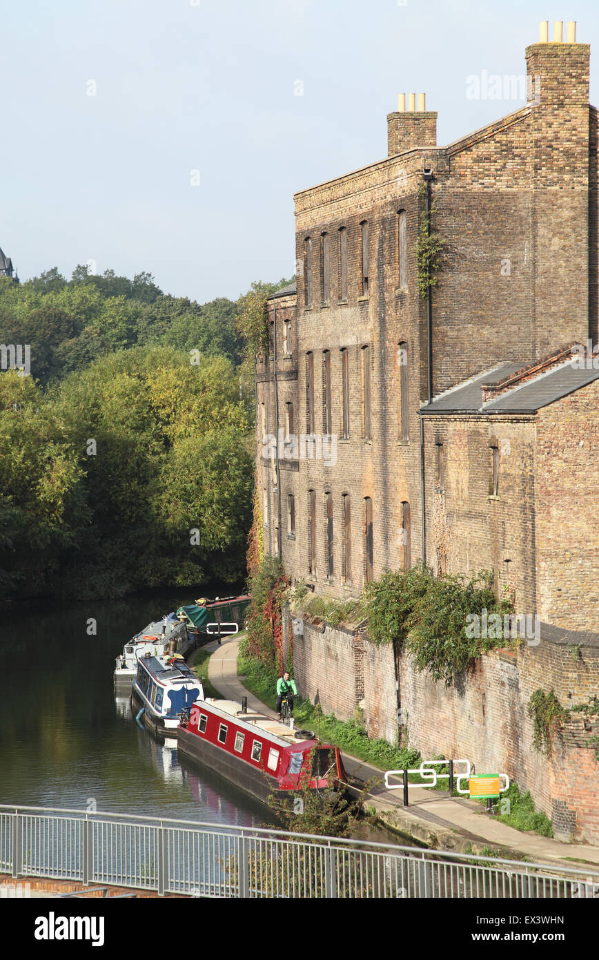 A cyclist passes moored narrow boats and Victorian buildings on the Regents Canal close to Kings Cross in central London Stock Photo