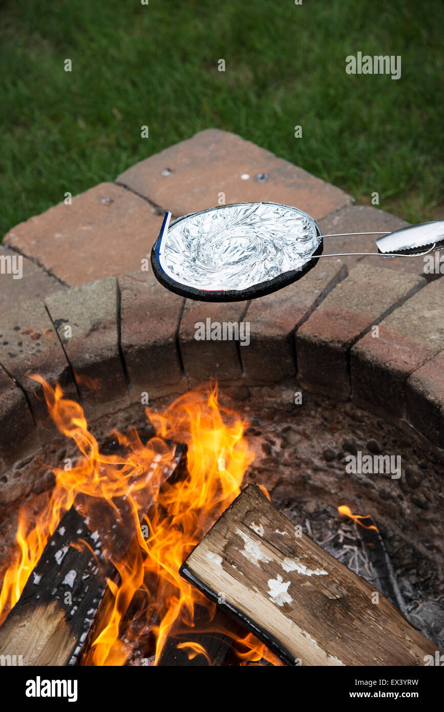 Cooking A Pan Of Popcorn In A Foil Covered Utensil Over A Garden