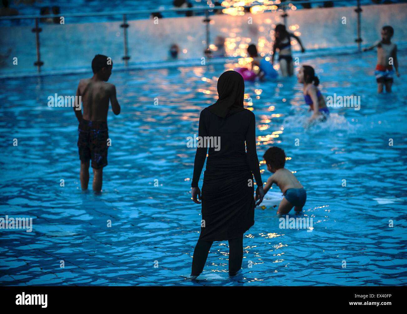 Berlin, Germany. 04th July, 2015. A fully clothed woman wearing a head  scarf stands in a pool of the summer swimming pool Hmboldthain in Berlin,  Germany, 04 July 2015. Visitors were able