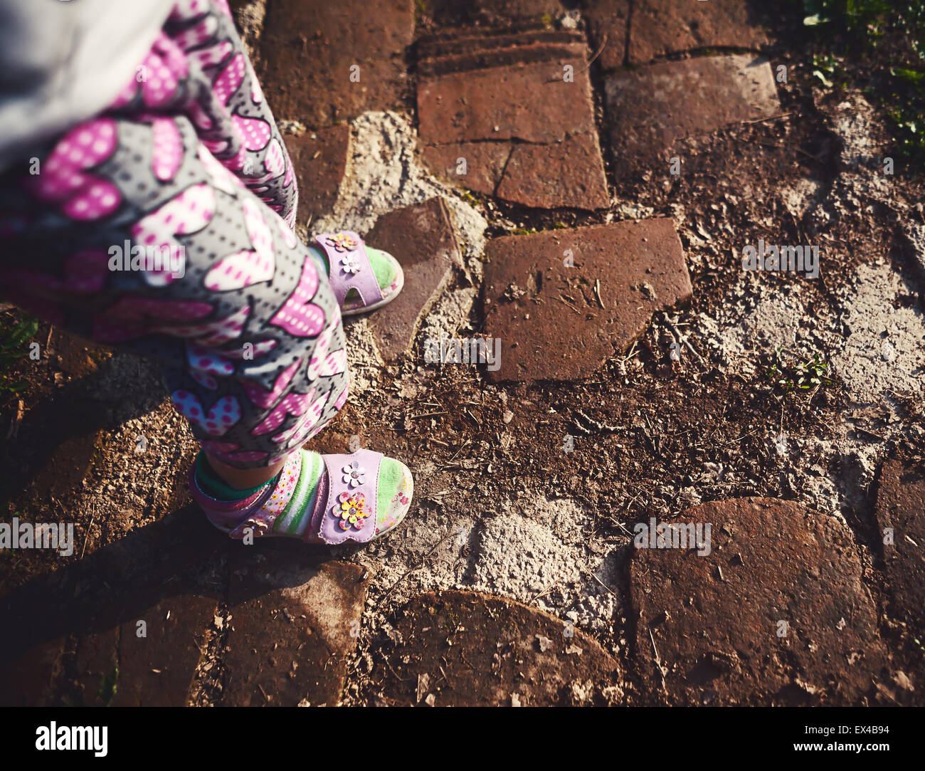Conceptual composition about child growth, details of baby girl legs standing on not so good road. Stock Photo