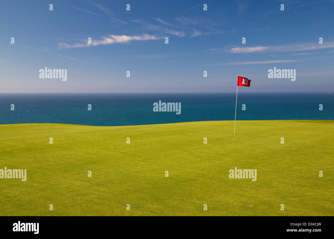 Red golf flag on Green with blue sea and sky behind. Stock Photo