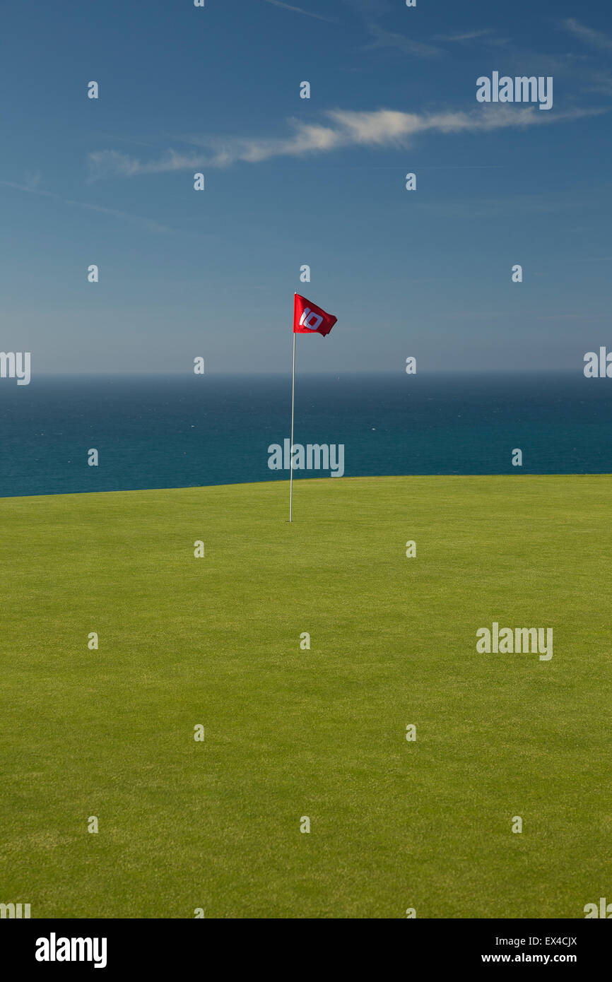 Red golf flag on Green with blue sea and sky behind. Stock Photo