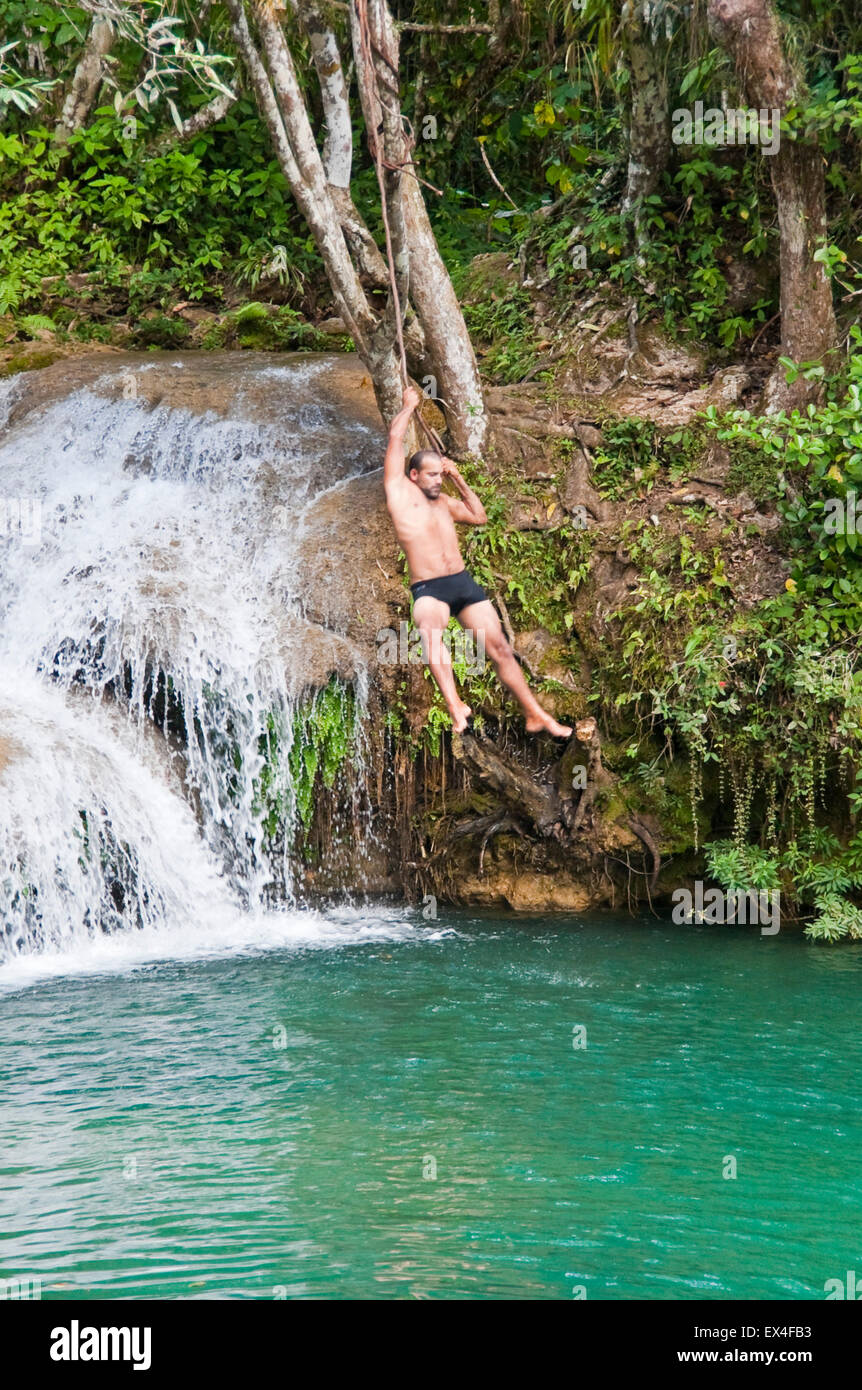 Vertical portrait of a tourist swinging from a liana into waterfalls in Topes de Collantes National Park in Cuba. Stock Photo