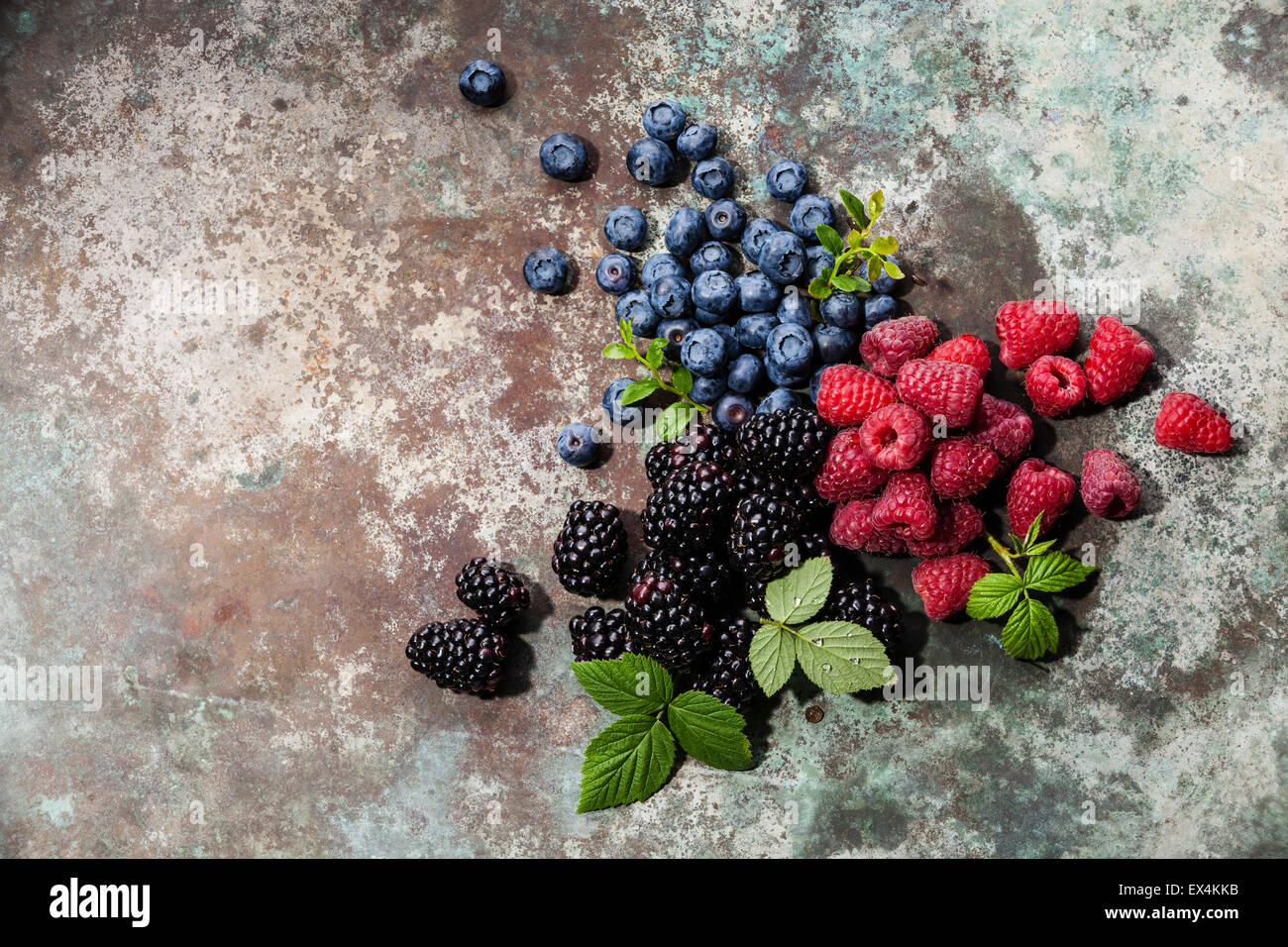 Assorted fresh berries with leaves on metal background Stock Photo
