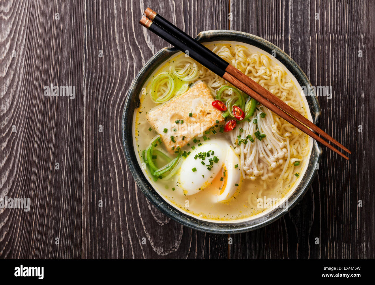 Asian Miso ramen noodles with egg, tofu and enoki in bowl on gray