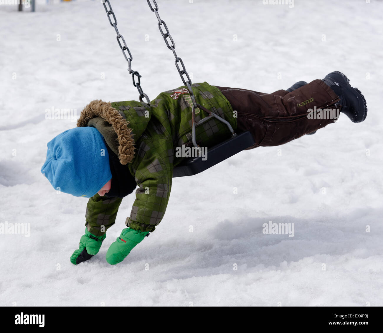 A young boy (3 yrs old) lying on a swing in winter in Quebec Stock Photo