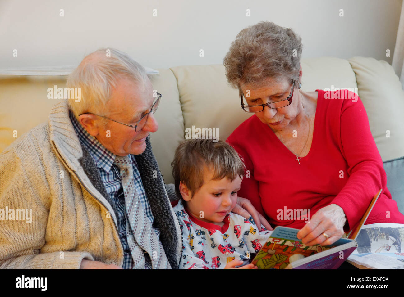 A toddler (3 yrs old) in pyjamas having a bedtime story with his grandparents Stock Photo