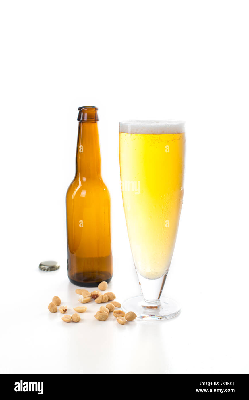 A full glass of beer with an empty brown beer bottle beside it, with some edible nuts in the foreground. Stock Photo