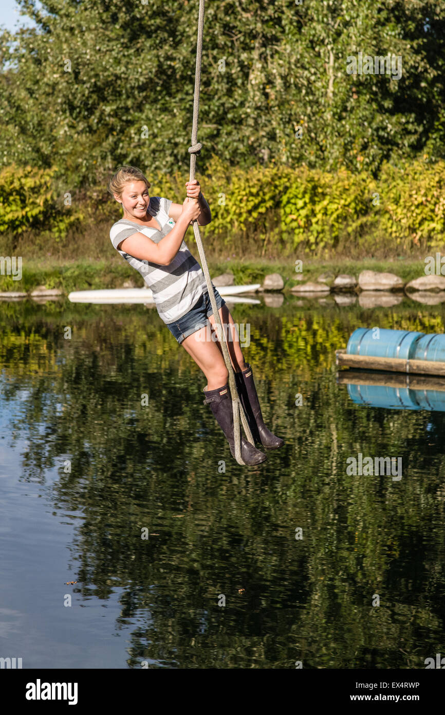 Young woman enjoying swinging on a rope swing over a farm pond in