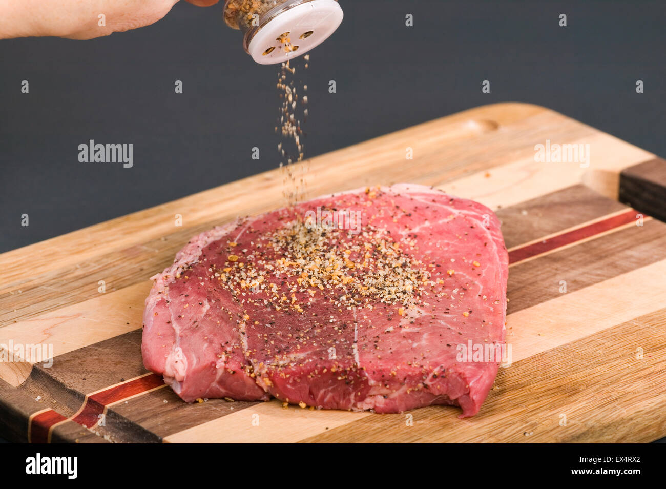 Meat tenderizer from a bottle being sprinkled on a steak sitting on a