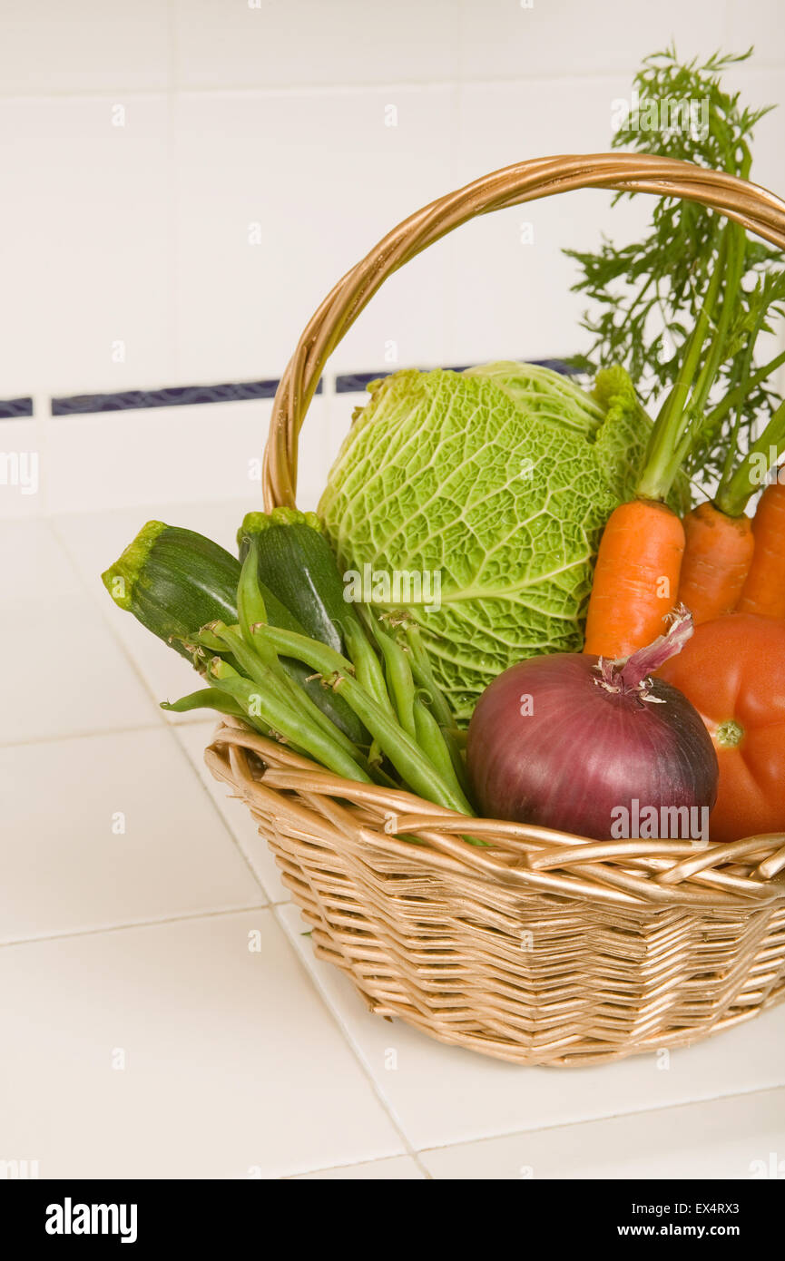 Basket of fresh produce in a kitchen with a white tile countertop Stock Photo