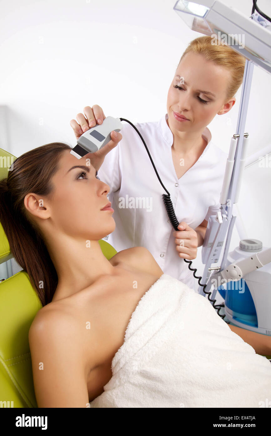 Portrait of attractive beautiful young adult brunette woman having a stimulating facial treatment from a therapist on the table  Stock Photo