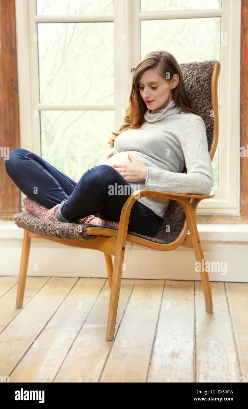 Pregnant Woman Sitting on Armchair Holding her Stomach Stock Photo