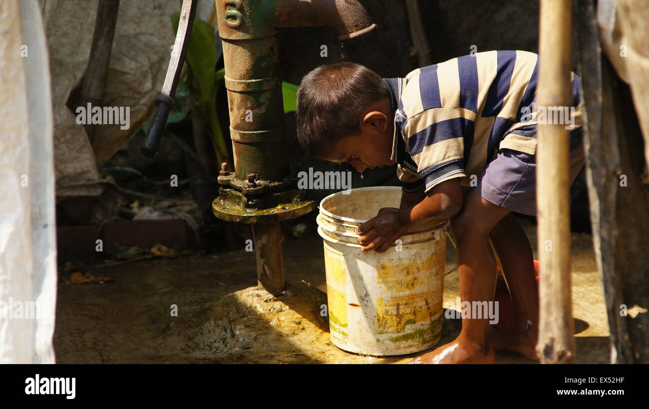 Hot in India. Little boy refeshing himself with cold water from the well. Stock Photo