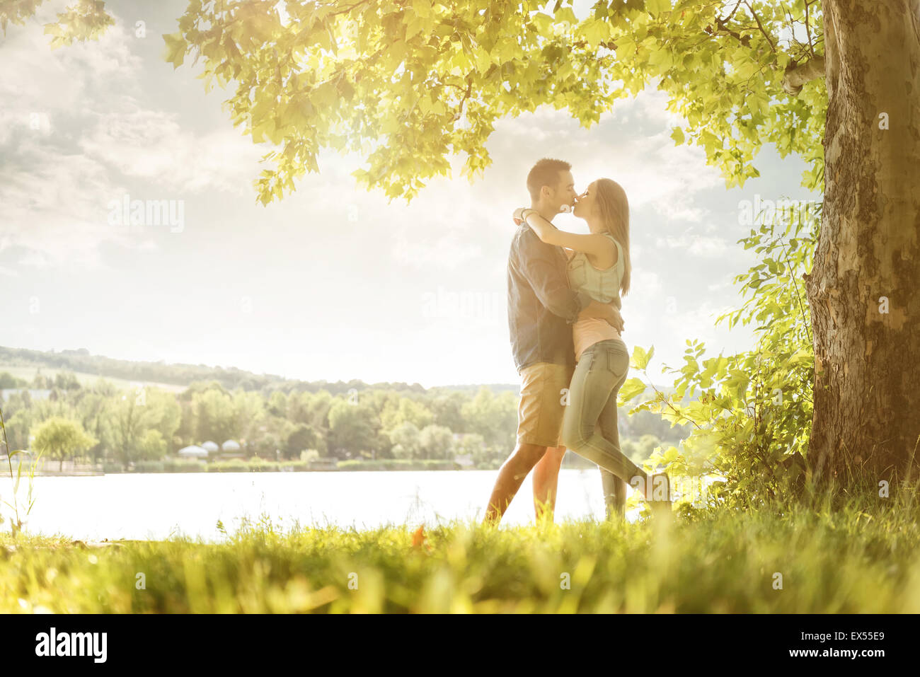 Couple in love on the lake, beneath the trees, kissing Stock Photo