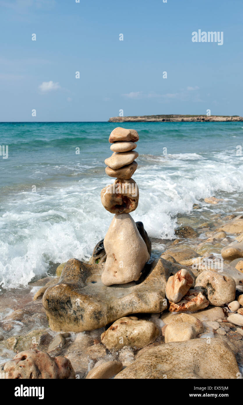 A pile of beach stones made into a sculpture tower on the shoreline of Sant Tomas beach on the island of Menorca Spain Stock Photo