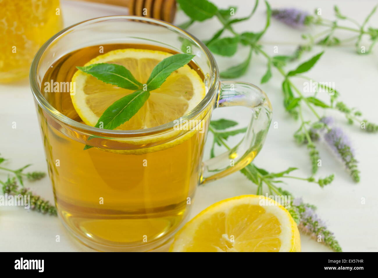 Cold healthy mint tea with lemon on a table with mint plant, honey,dipper and dessert Stock Photo