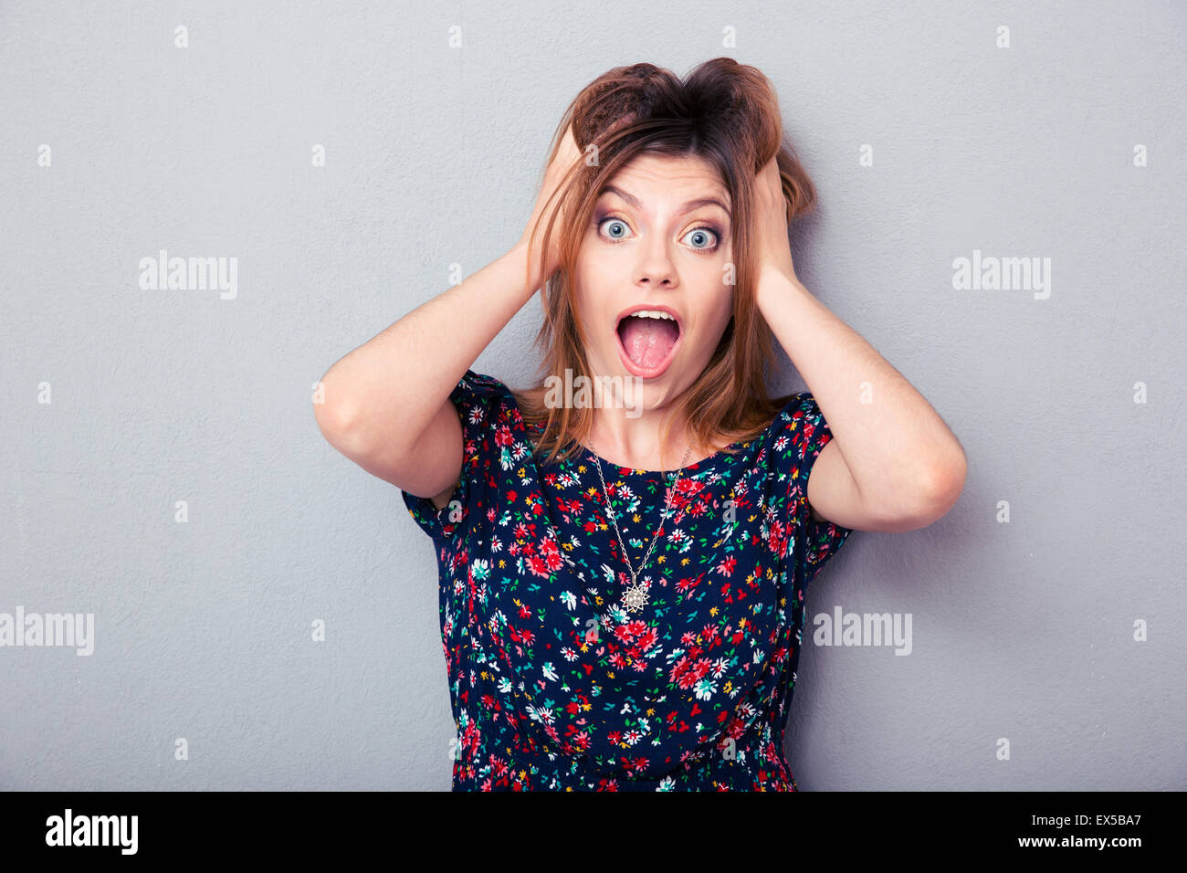 Surprised young woman screaming over gray background. Looking at camera ...