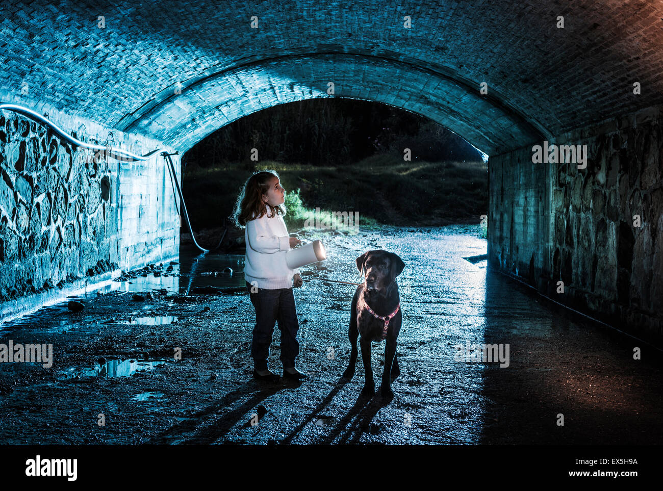 Little girl and her pet dog in a dark tunnel. Stock Photo