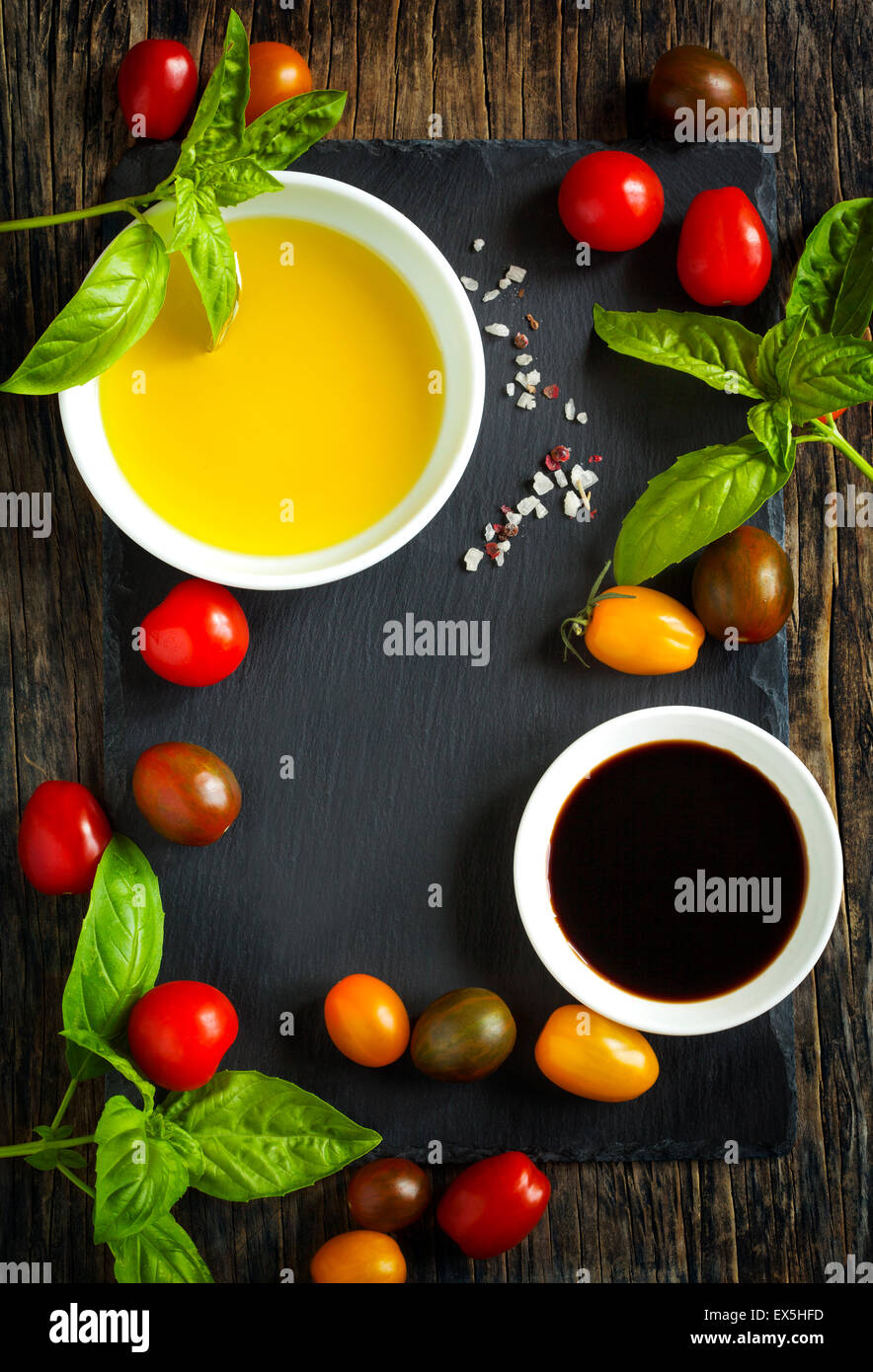 Fresh tomatoes, basil, olive oil and balsamic vinegar on wooden background with black board, top view Stock Photo