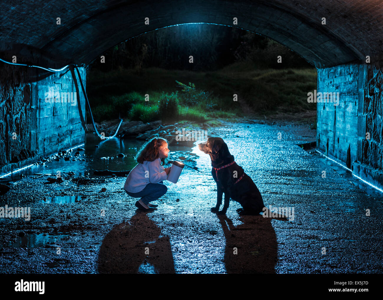 Little girl and her pet dog in a dark tunnel. Stock Photo