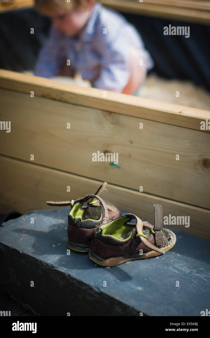 boys shoes sitting at side of home garden sand pit in summer while he plays Stock Photo