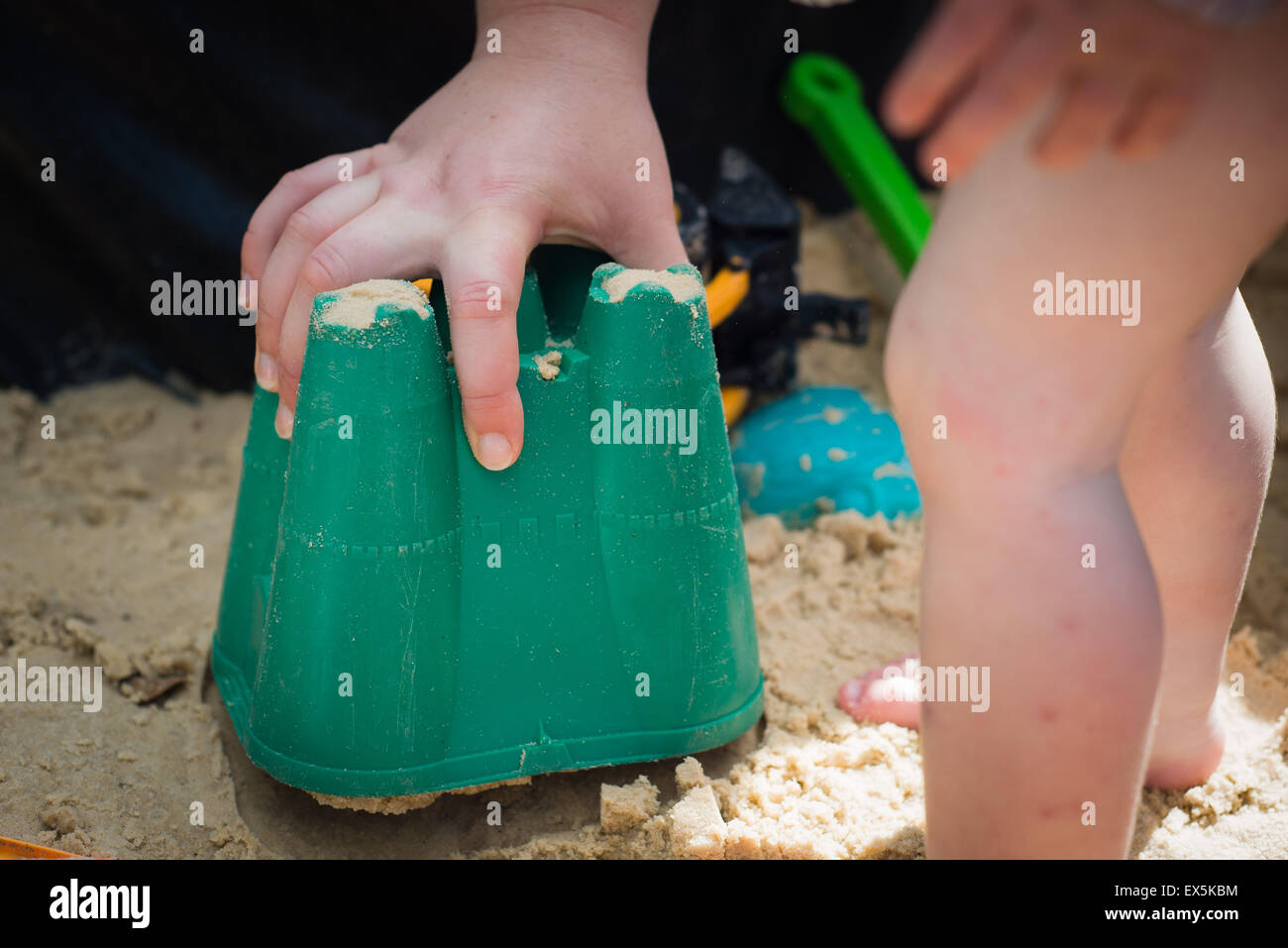 adult helping child lift bucket to reveal sand castle Stock Photo